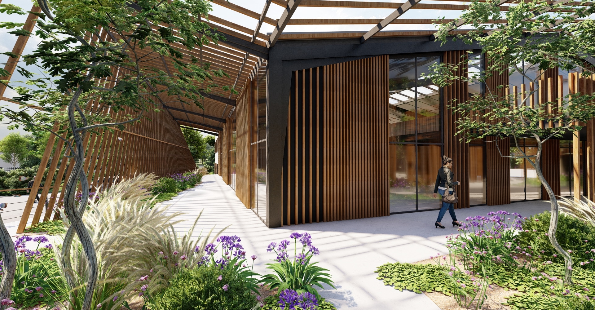 Façade bois d'une architecture moderne avec pergola. Une femme marche sur la passerelle bordée de fleurs violettes et de grands arbres.
