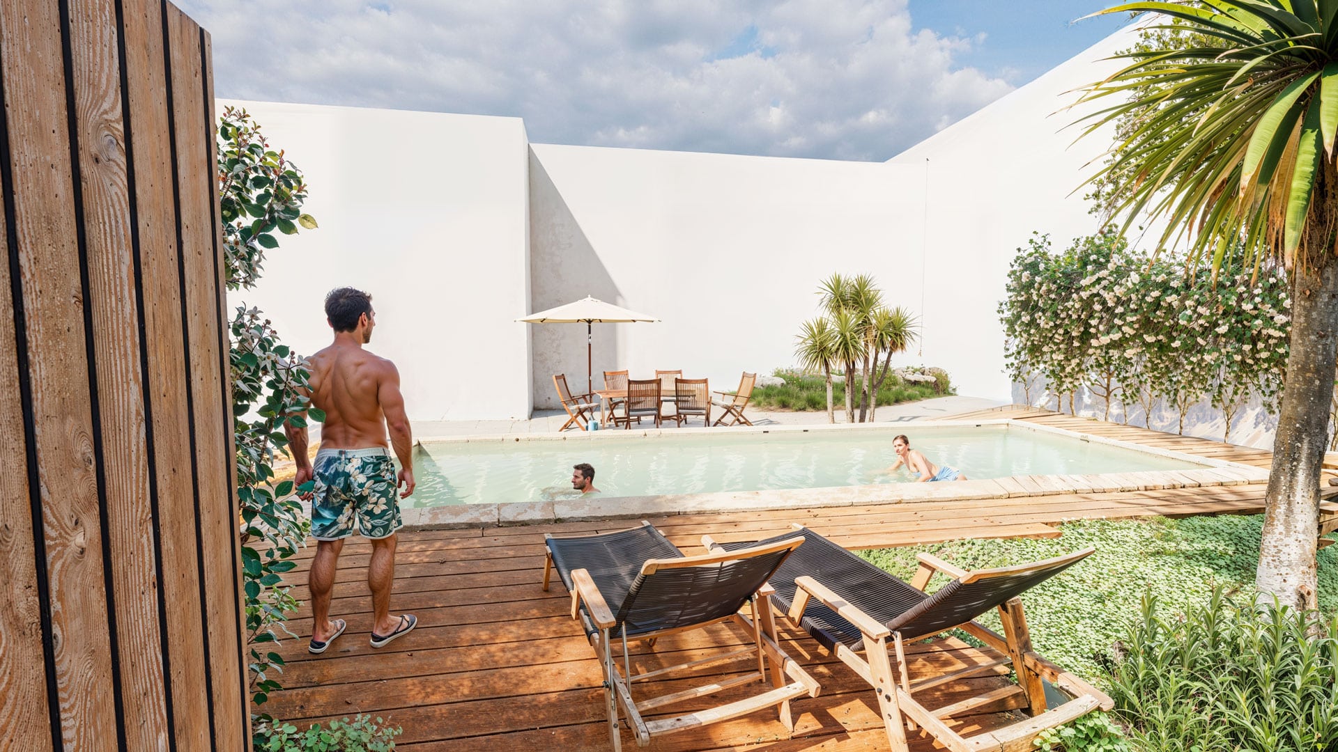 Groupe d'amis profitant d'une piscine moderne avec terrasse en bois et transats dans une villa luxueuse ensoleillée.