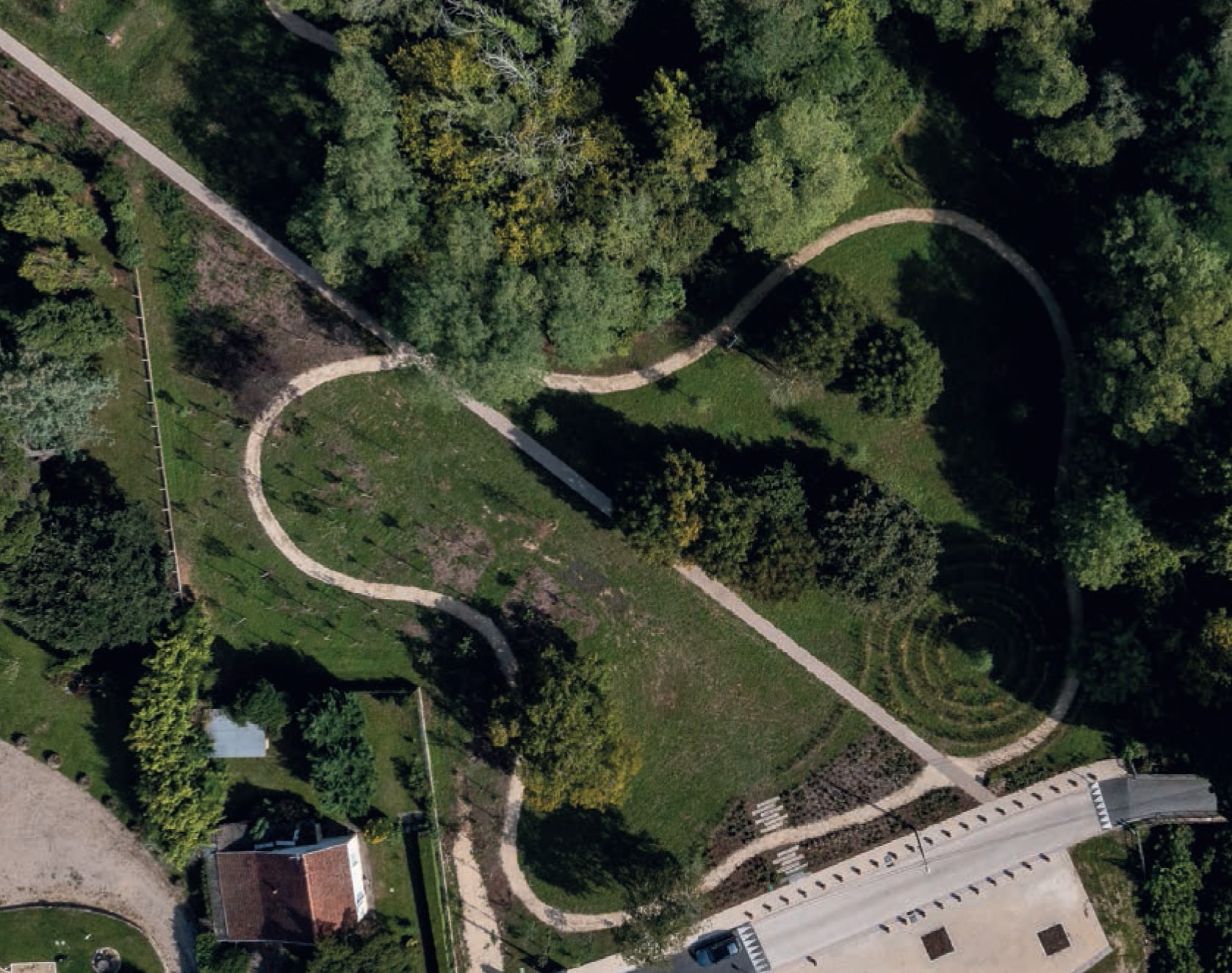Vue aérienne d'un parc avec sentiers sinueux, labyrinthe végétal et boisement dense.