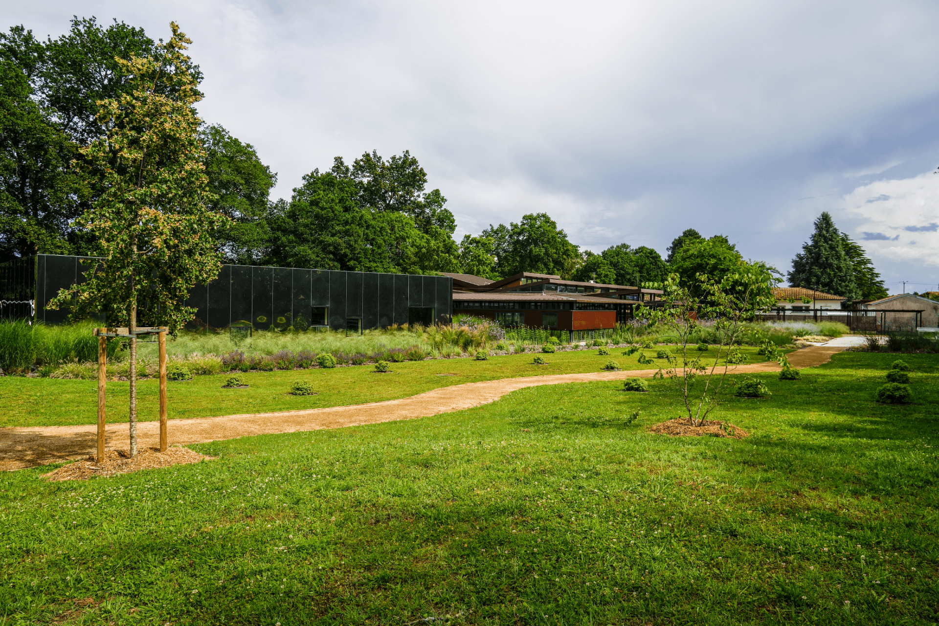 Architecture moderne dans un parc paysager avec sentier sinueux et pelouse verdoyante sous un ciel nuageux.