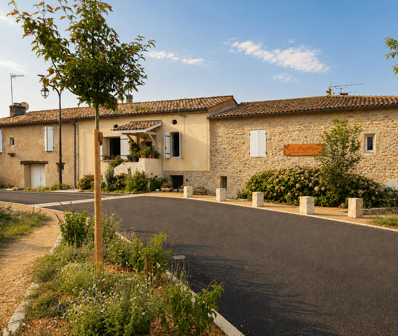 Maison en pierre "Le Papillon", volets blancs et hydrangeas sous un ciel clair ensoleillé.