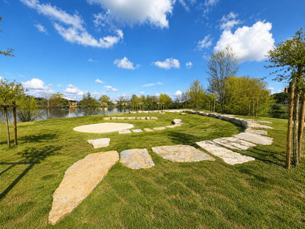 Jardin paysager : chemin de pierre et étang au soleil Chemin en dalles de pierre dans un jardin paysager verdoyant bordé d'un étang sous un ciel bleu.