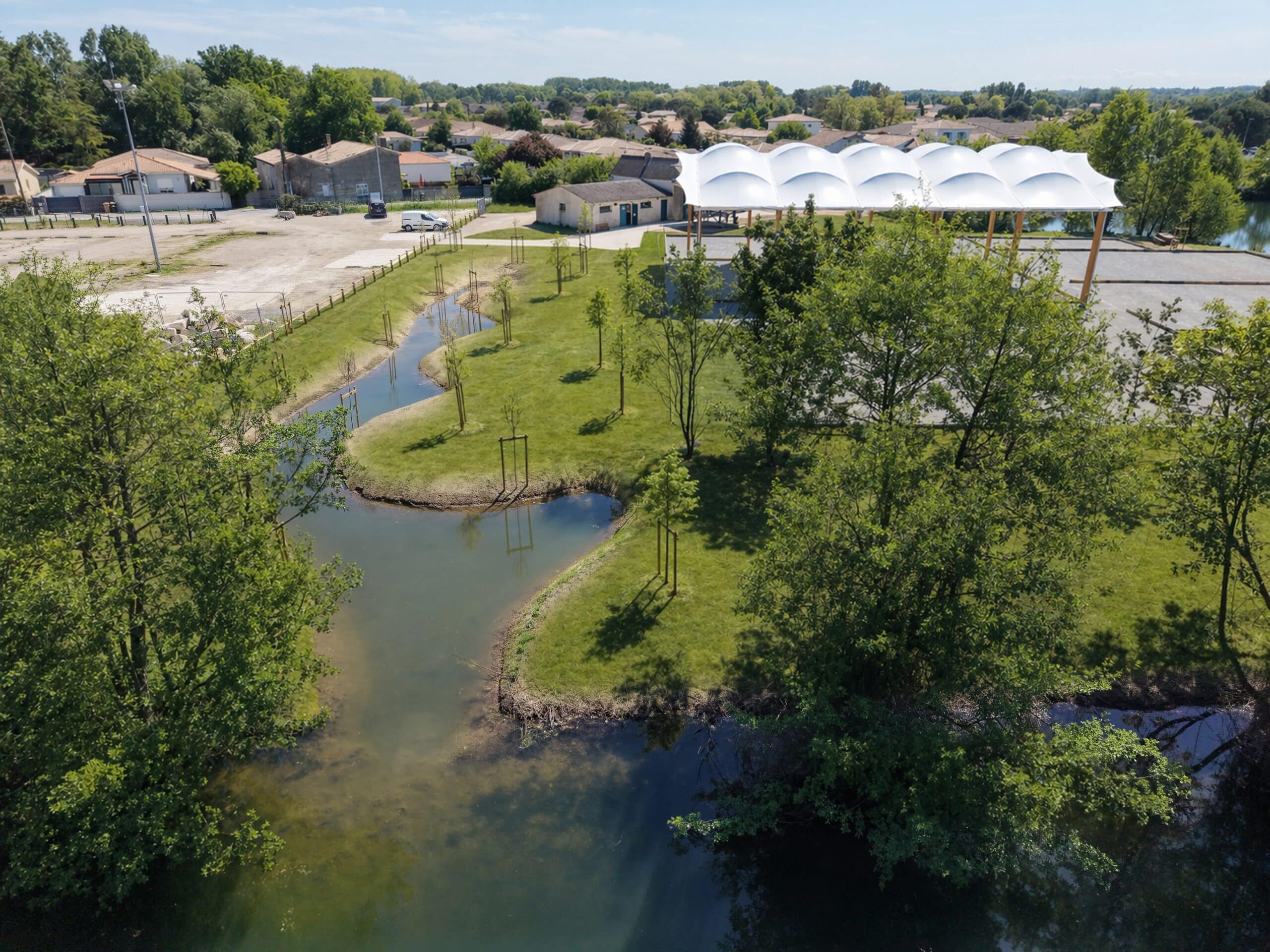 Bassin sinueux, pelouse verte et structure blanche moderne dans un parc paysager ensoleillé.