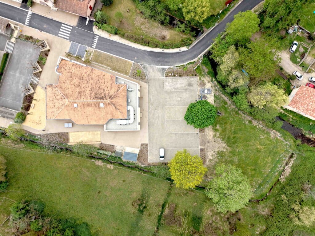Vue Aérienne Bâtiment Moderne avec Parking et Verdure Vue aérienne d'un bâtiment au toit de tuiles avec son parking et ses jardins verdoyants.