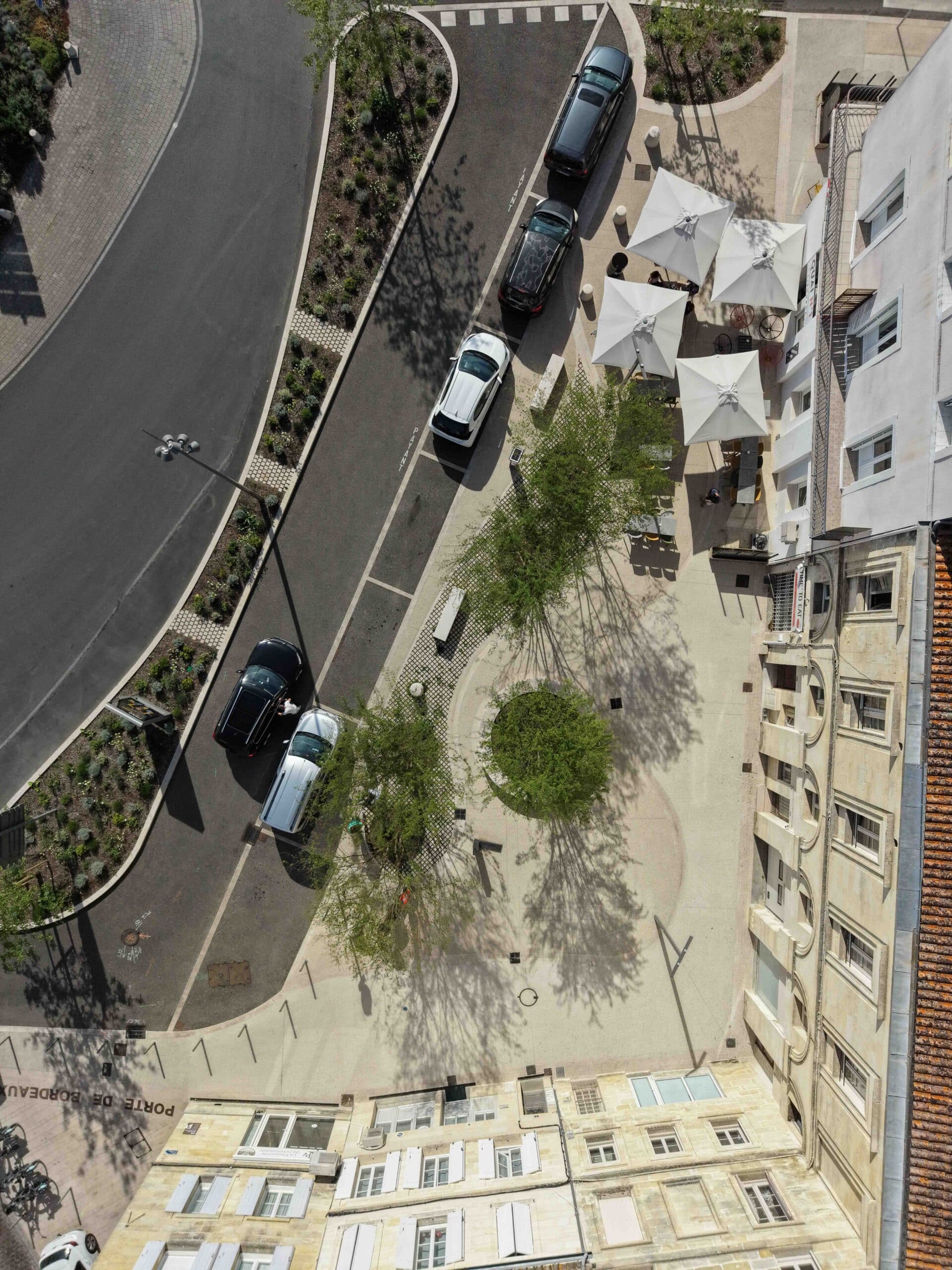 Place Porte de Bordeaux vue d'en haut avec ses terrasses de café, arbres et voitures garées sur pavés.